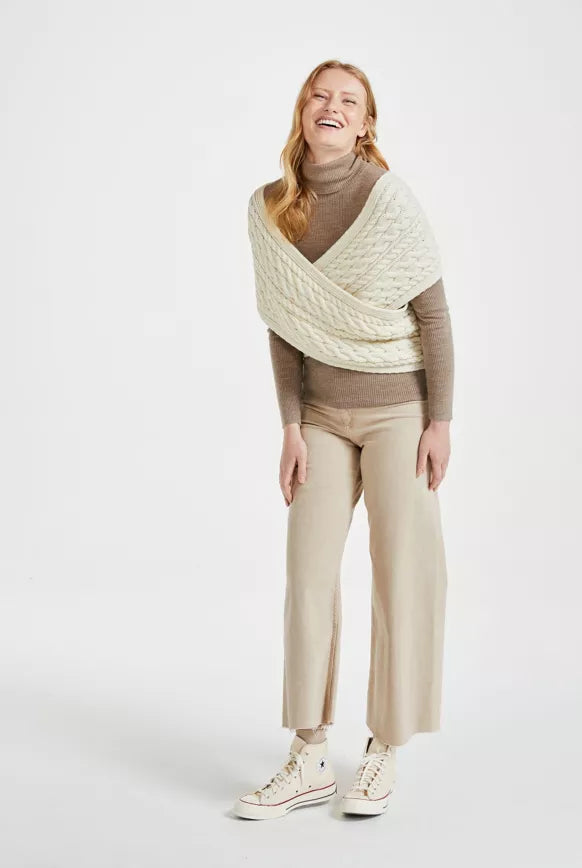 Een gewikkelde witte gebreide sjaal wordt gedragen samen met een beige pantalon en coltrui. 