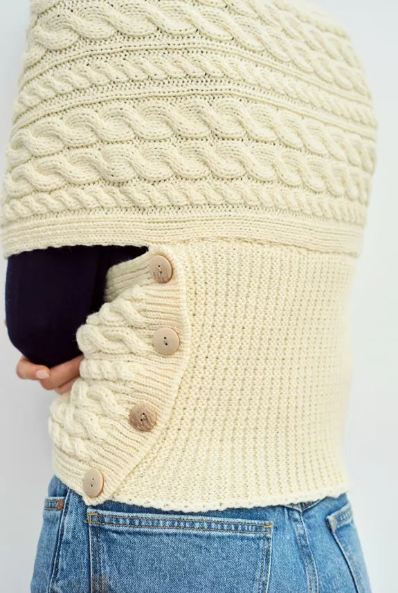 Ingezoomd beeld van het zij aanzicht van een gewikkelde sjaal top. De sjaal sluit om de middel door vier naturel gekleurde knopen. 