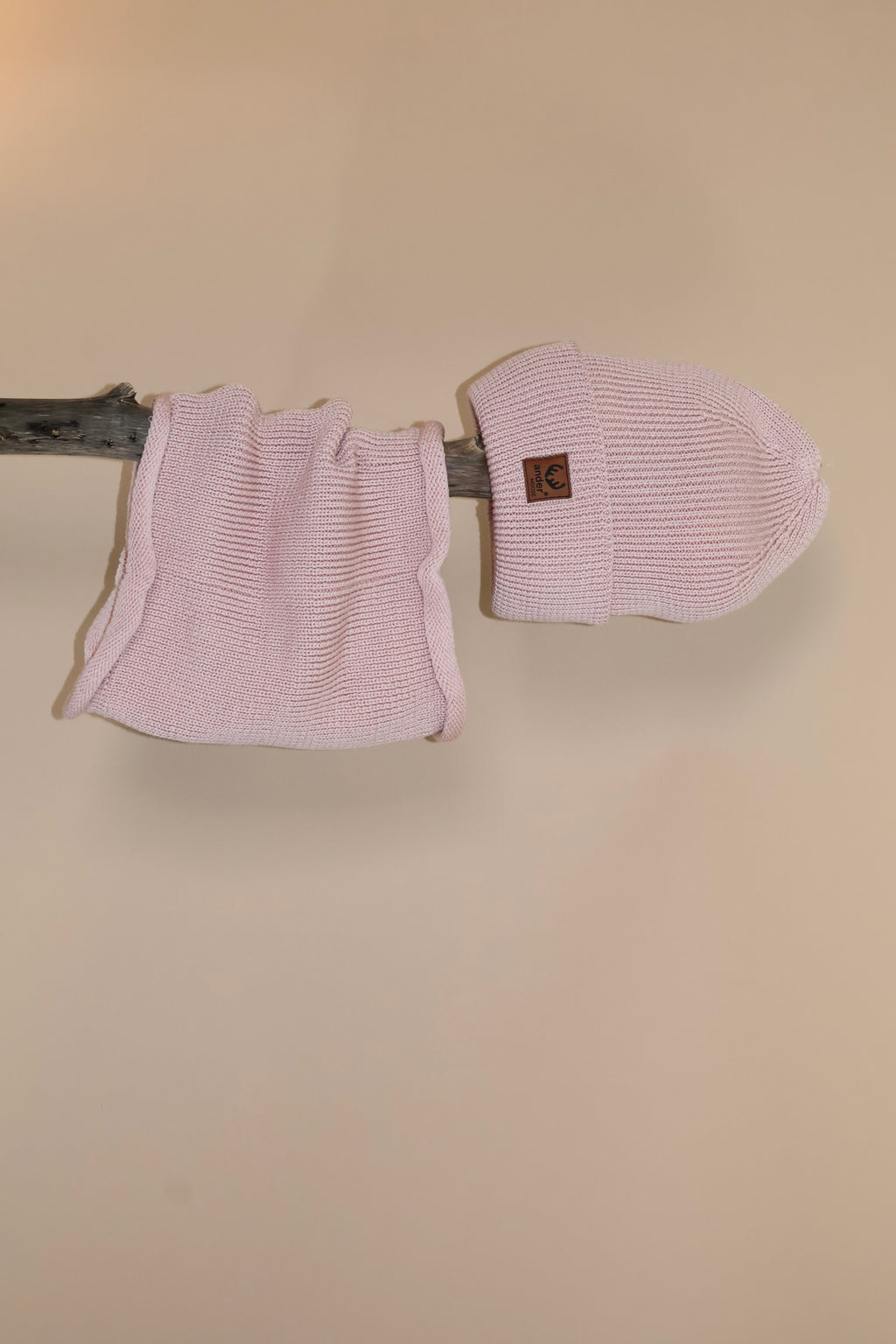 Op een stok gepresenteerd, hangt een col en op de uiteinde een bijpassende muts. De set is roze gekleurd en gebreid.