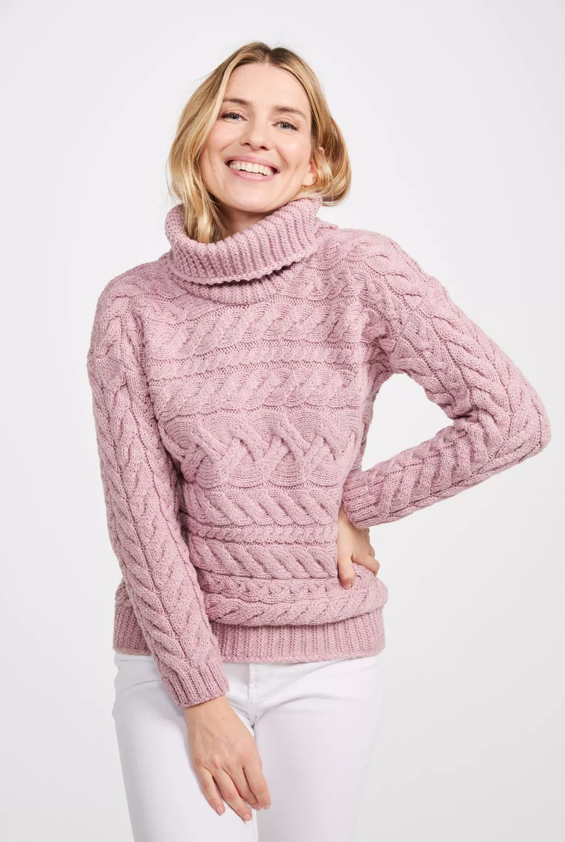 Vrouw draagt een grof gebreide roze coltrui. Het bovenstuk heeft meerdere soorten kabels horizontaal gebreid.
