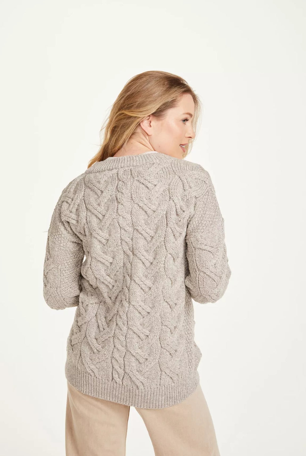 Beeld van een vrouw van achteren. Ze draagt een beige kabelgebreid vest. Het kledingstuk valt over de heupen.