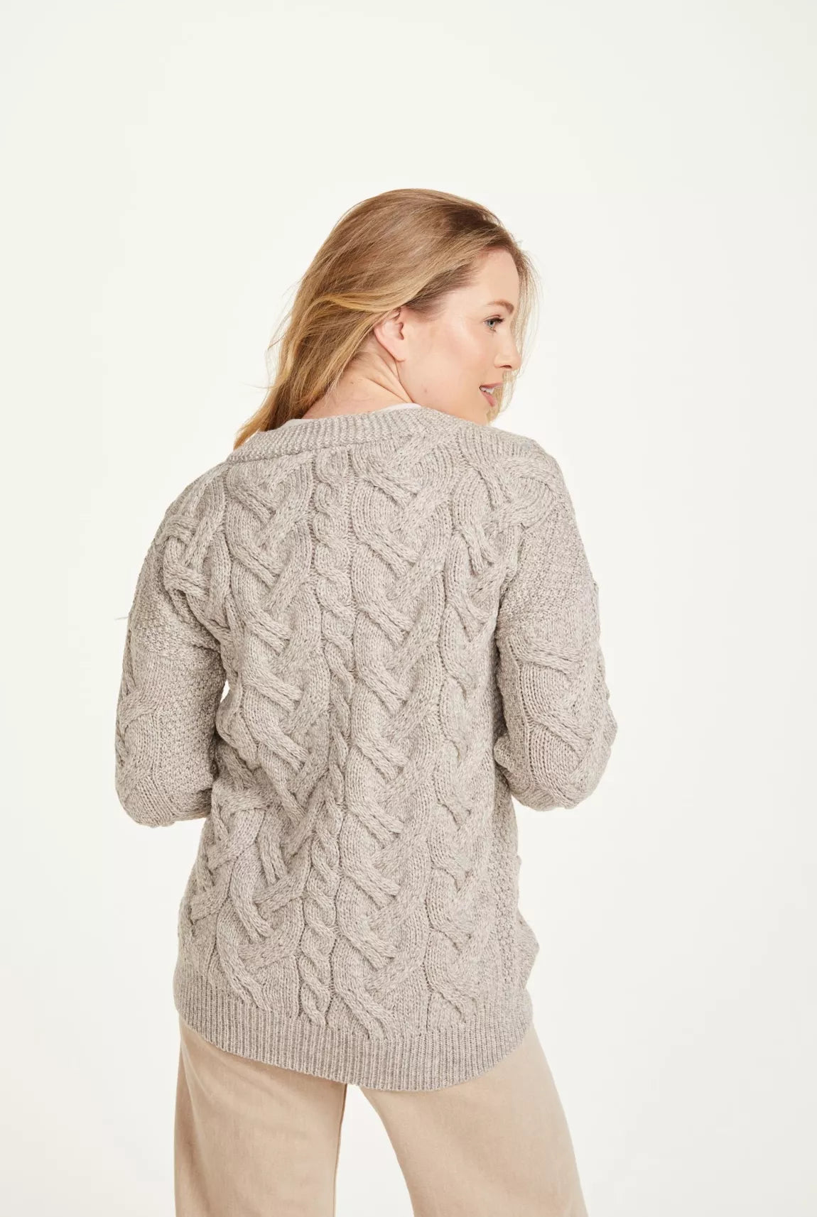 Beeld van een vrouw van achteren. Ze draagt een beige kabelgebreid vest. Het kledingstuk valt over de heupen.