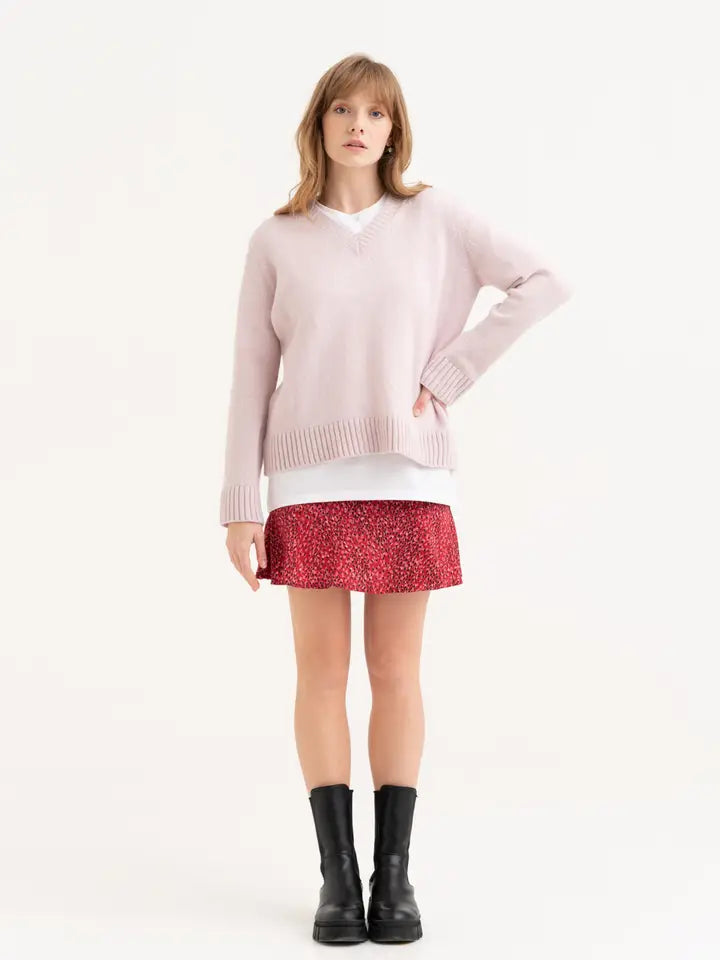 Een roze gebreide sweater wordt gedragen op een rood rokje. Het beeld benadrukt dat de lengte van de trui op de heup valt.