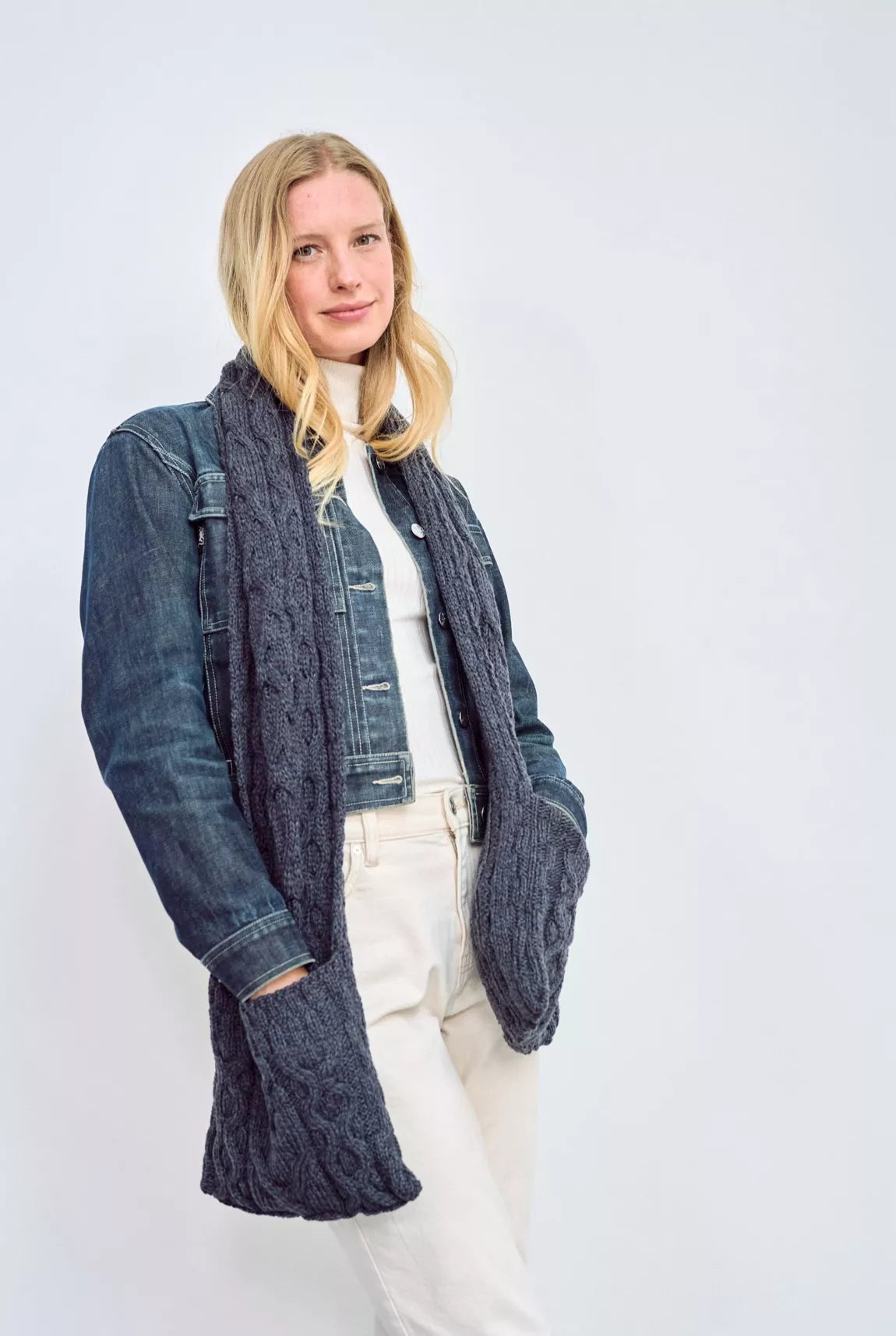 Vrouw draagt een outfit met een grote donker blauwe sjaal met zakken. Haar handen accentueren dit praktische details.