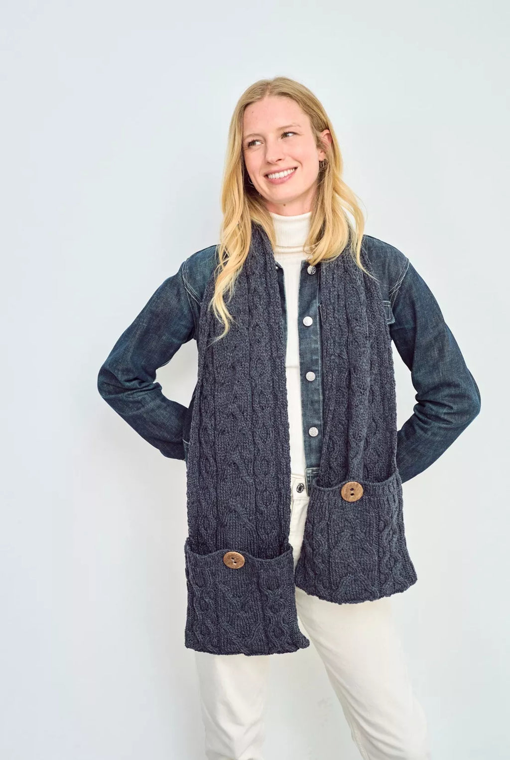 Een kabel gebreide sjaal in een donker blauwe kleur. De focus ligt op de door een knoop gesloten zak op de uiteinden van deze winter accessoire.