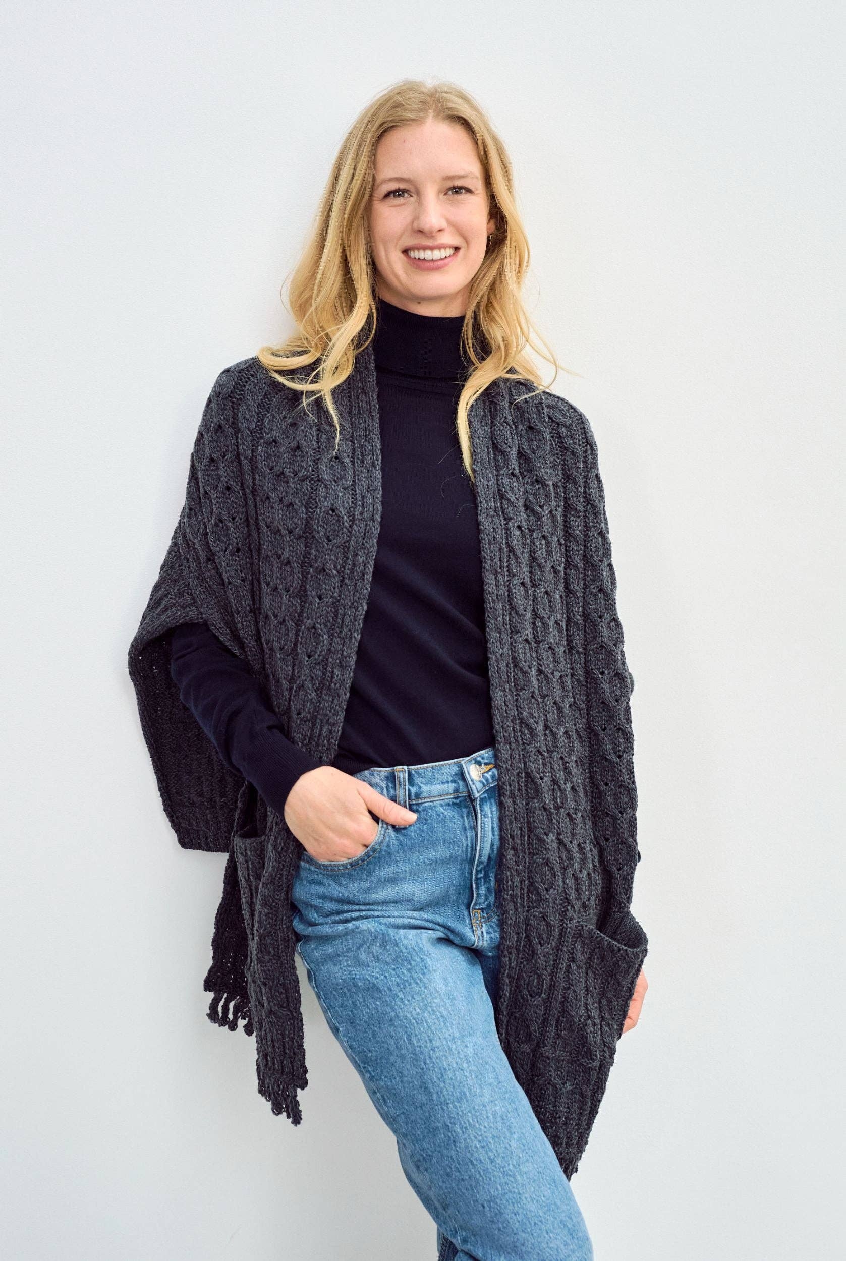 Een grijze ruime sjaal wordt gedragen op een casual outfit. De omslagdoek is grof gebreid en heeft twee zakken.