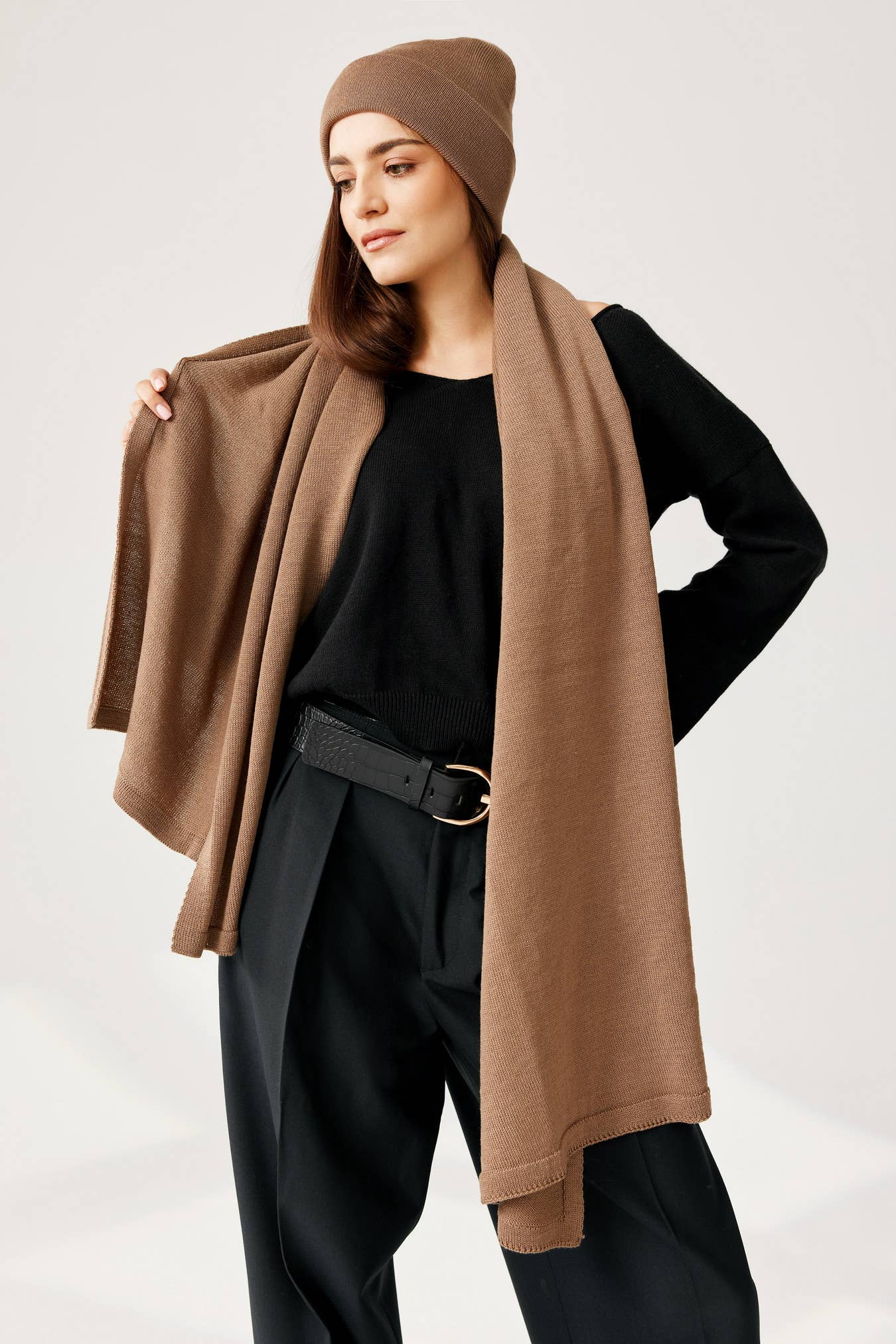 Vrouw draagt zwarte trui en broek gecombineerd met kameel kleurige sjaal en muts.