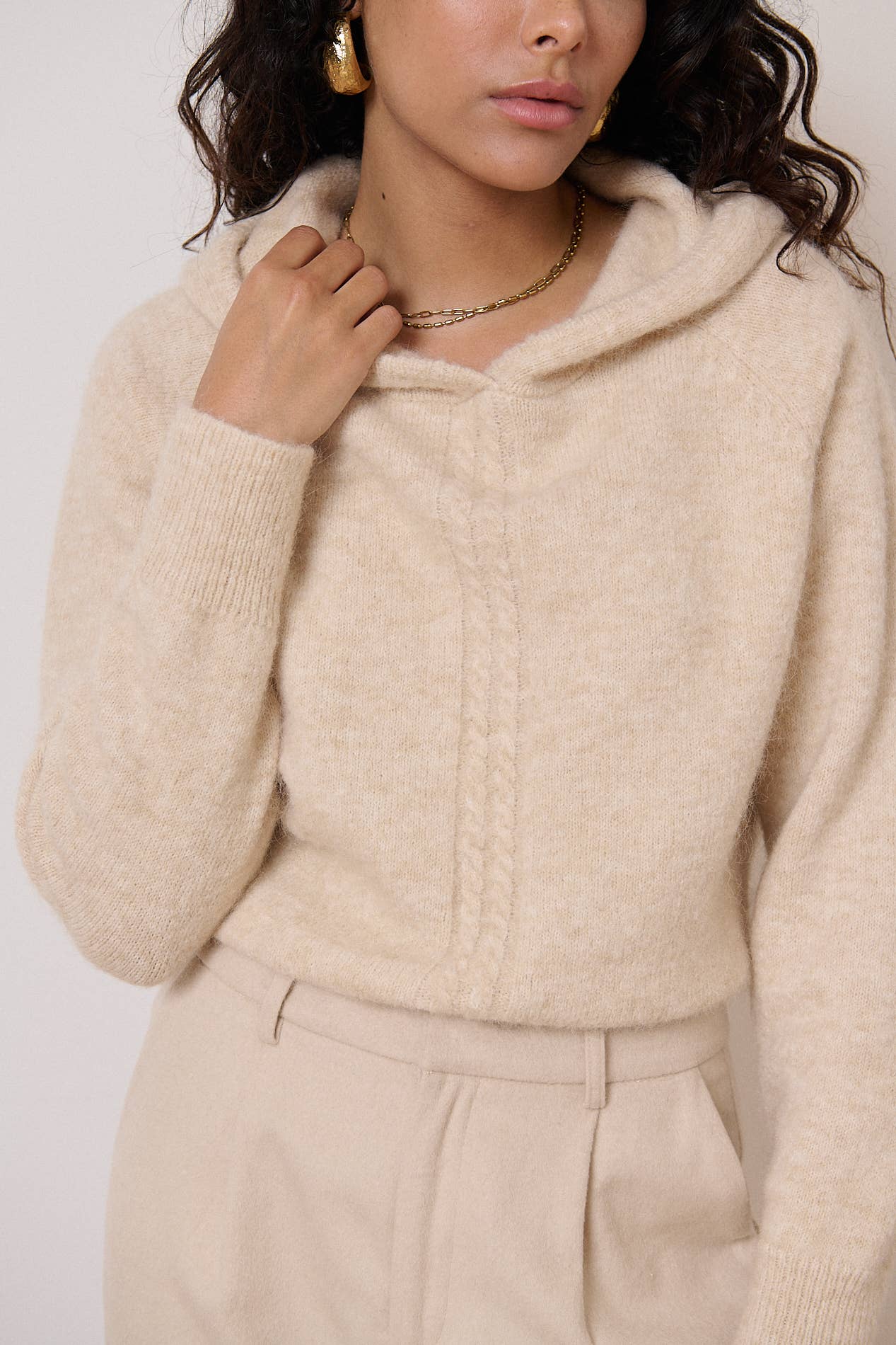 Een beige trui met een capuchon, brede boorden en een kabelgebreid detail op het voorpand.