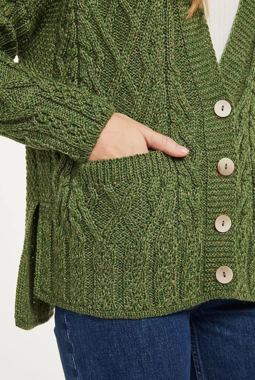 Ingezoomd beeld van een vrouw met een groen gebreid vest aan. De focus ligt op de zak, knoopsluiting en de split in de zijnaad.