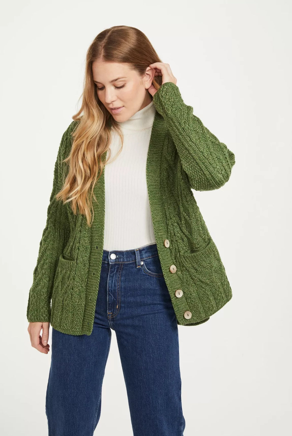 Een groen gebreid vest wordt gedragen door een vrouw samen met een witte trui en jeans. De sluiting bestaat uit vier knopen en het model is verfraaid met twee zakken op het voorpand.