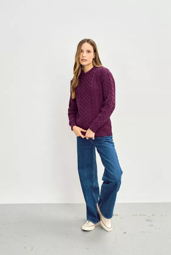 Vrouw draagt een paarse kabeltrui met ronde hals, gecombineerd met donkerblauwe jeans en witte sneakers, voor een casual look.