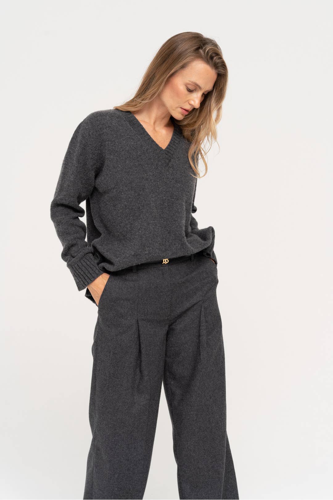 Een grijze wollige outfit waarbij de trui een V-hals heeft en de broek wordt gedragen met een zwarte riem.