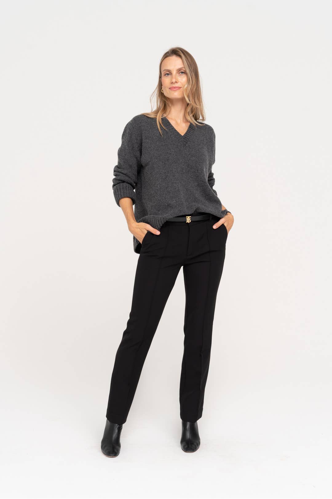 Vrouw draagt zwarte pantalon met grijze trui. Gebreid V-hals model met opgestroopte mouwen