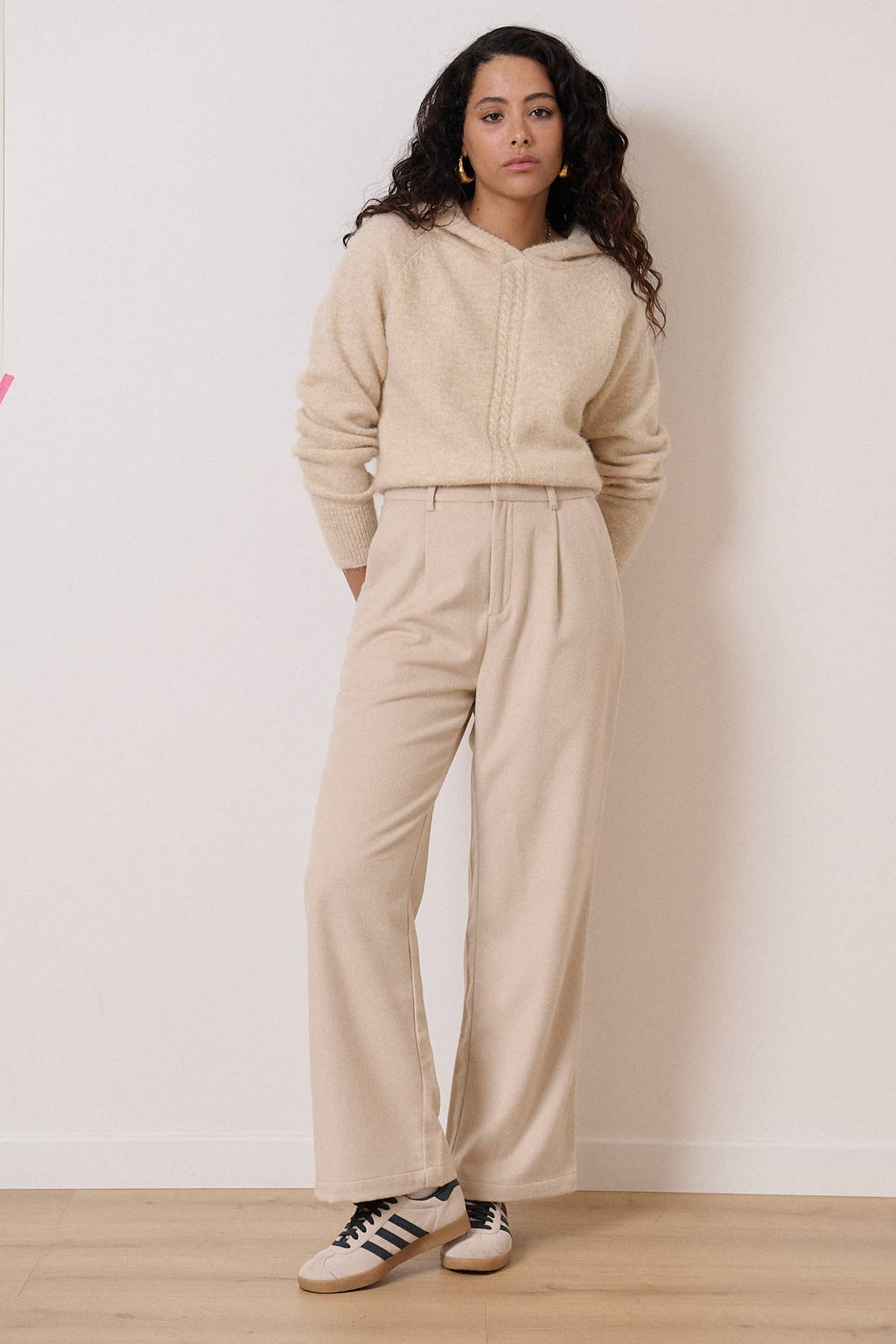 Een beige outfit wordt gedragen waarbij de focus ligt op een fijn gebreide trui.